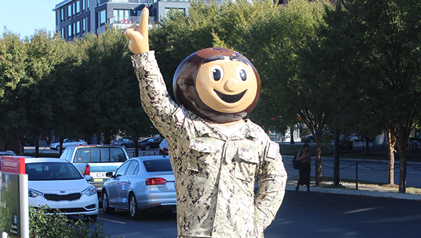 Ohio State Buckeyes mascot wearing a camouflage military uniform stands outdoors on a campus street.