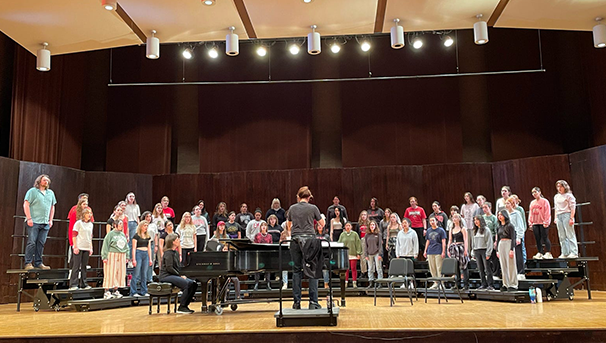 Women's Glee Club members practicing on stage. They stand on risers