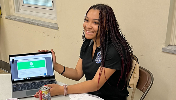 Student holding laptop while smiling sitting at table