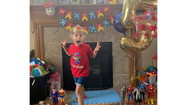 Child standing in front of fireplace with balloons and party supplies for 5th birthday