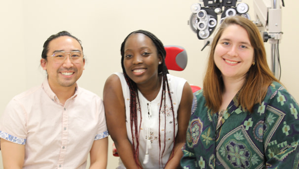 Three individuals sit in an examining room, smiling at the camera