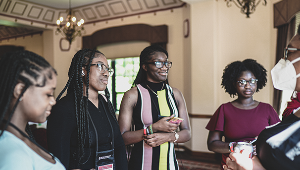 Individuals standing in a group listening to a speaker