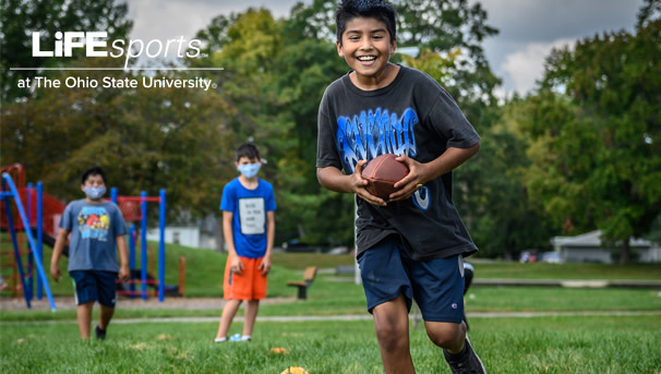 One boy stands before two others, holding a football in the center of his chest