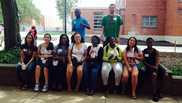 Group of students smiling for a photo outside sitting on a cement block