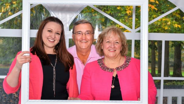 Three individuals holding a picture frame prop around their heads while smiling for a photo