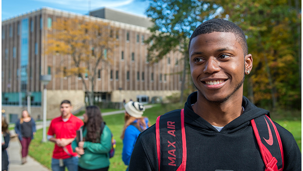 A student standing in camera focus with Ovalwood Hall on the Mansfield campus behind him.