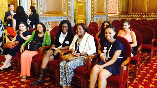 Group of students sitting in chairs inside a building smiling for a photo