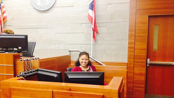 Student smiling for a photo inside a courtroom behind a desk