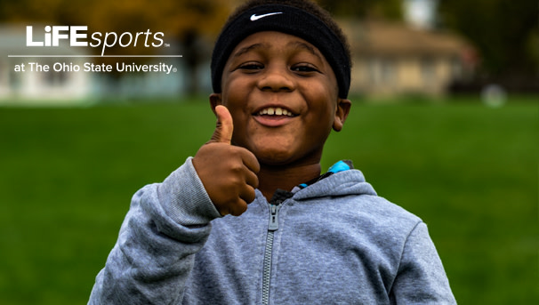 A young student holds up his thumb with a small smile