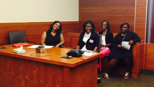 Four individuals sitting in a court room behind a desk smiling for a photo