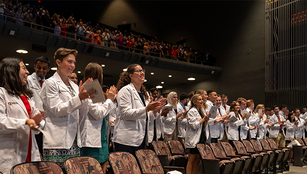 Group of students wearing their white coats at a ceremony inside