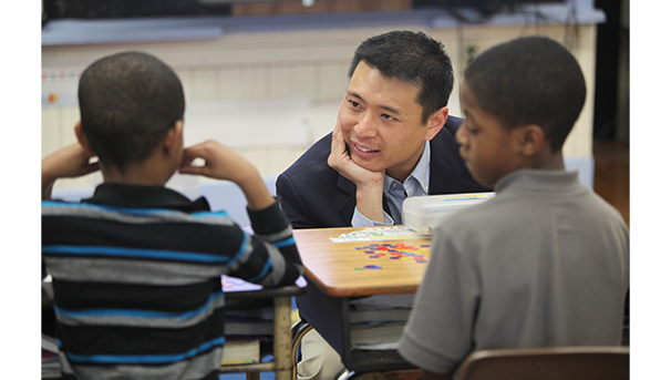 A man talks to two young boys at their school desks