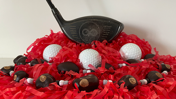 Driver golf club sitting on a red pom pom with three golf balls and a Buckeye necklace