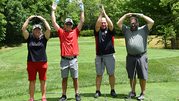 Four individuals holding their arms up to spell OHIO on the tee box of a golf course