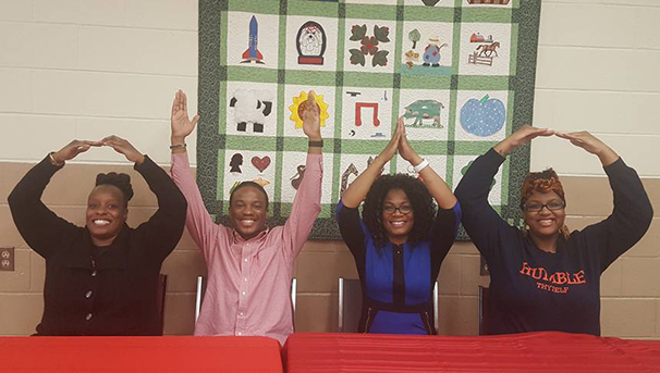 Four individuals sitting at a table holding their arms up for OHIO