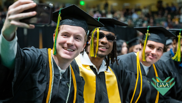 UAA graduates take a joyful selfie at commencement, celebrating student success.