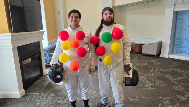 Two fencers in their uniforms with balloons taped to the uniforms
