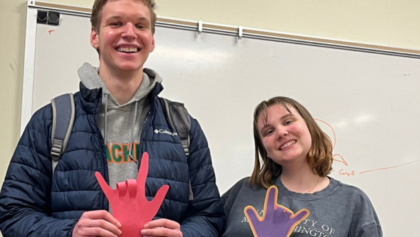 Two students holding paper hands showing sign language