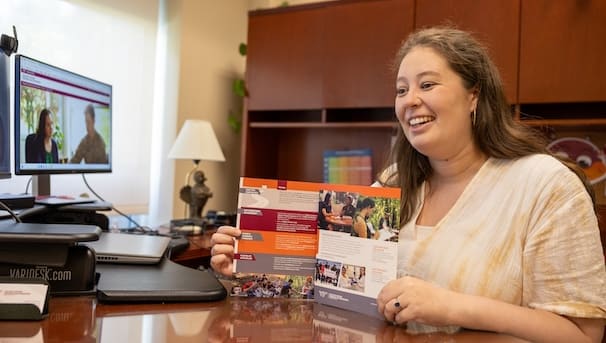 Woman with brown hair holds a maroon and orange colored booklet.