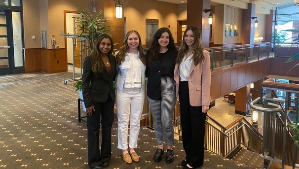 Four students in business professional attire smiling for a photo inside