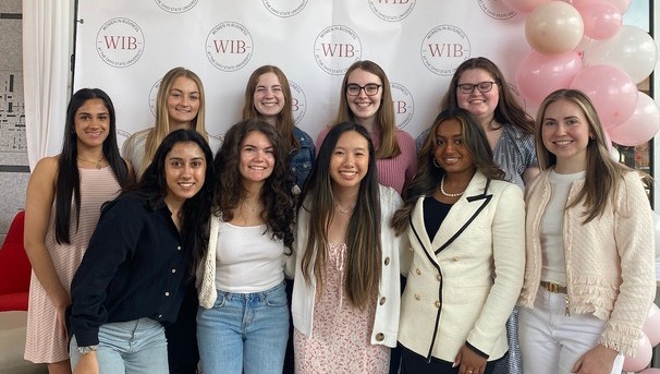 Group of students standing in front of a Women in Business backdrop with balloons