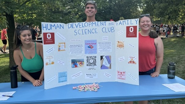 Three students standing behind a table at involvement fair with poster board