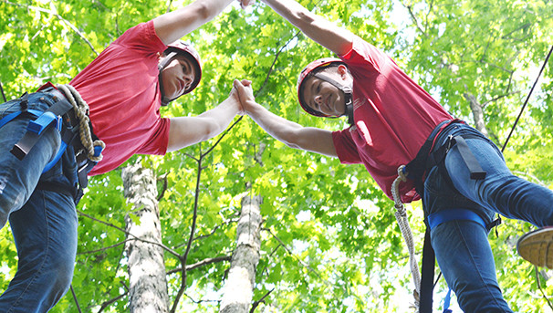 Two campers holding onto each other hand's. They are balancing on trees