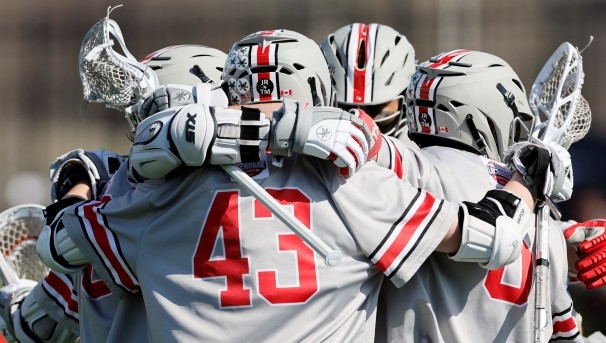 Group of lacrosse players in grey uniforms huddle during a game