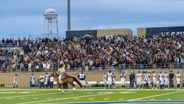 Maggie the Aggie riding a horse through Stadium in front of cheering crowd at football game.