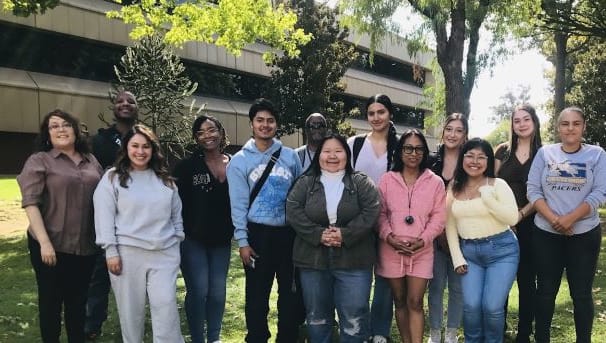 13 individuals smiling for a photo on campus