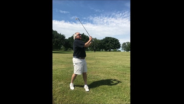 A man standing on a golf course. He holds a golfclub up in the air while also looking at it