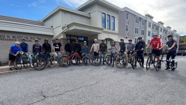 Several students posing with their bikes outside of a dorm.