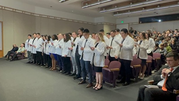 Physical therapy students standing in their white coats and reading the oath.