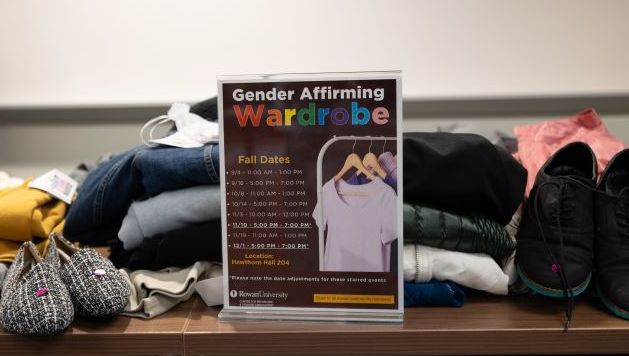 Table of clothes and shoes with signage for the gender affirming wardrobe with dates and times.