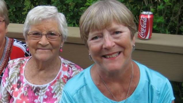 Jill Vanuch and another woman sit outside, a light brown wood fence behind them