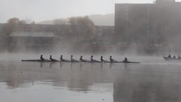 Students rowing on a foggy river.