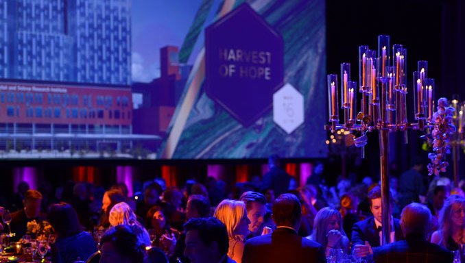 2019 Dinner Guests sit at their round tables. At the front of the room is a large projection