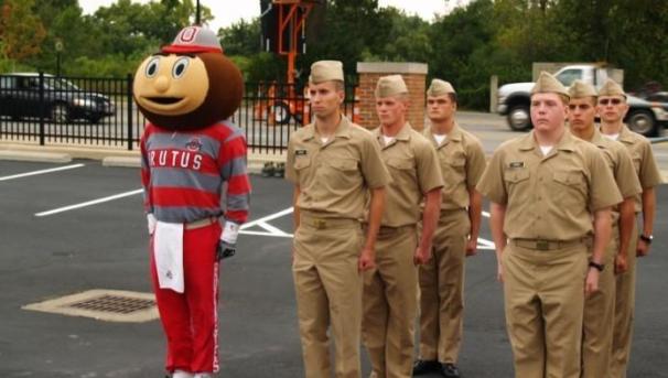 Brutus Buckeye stands beside ROTC cadets marching in formation across a parking lot