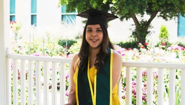 Grisol Lupita Ramirez wearing a cap and gown, smiling and seated near flowers on a sunny day.