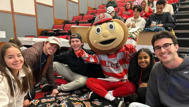 Group of students sitting in a room with Brutus looking up smiling at the camera