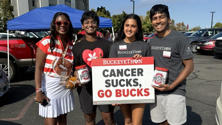 Individuals holding a Buckeye Thon sign that says "Cancer Sucks, Go Bucks"