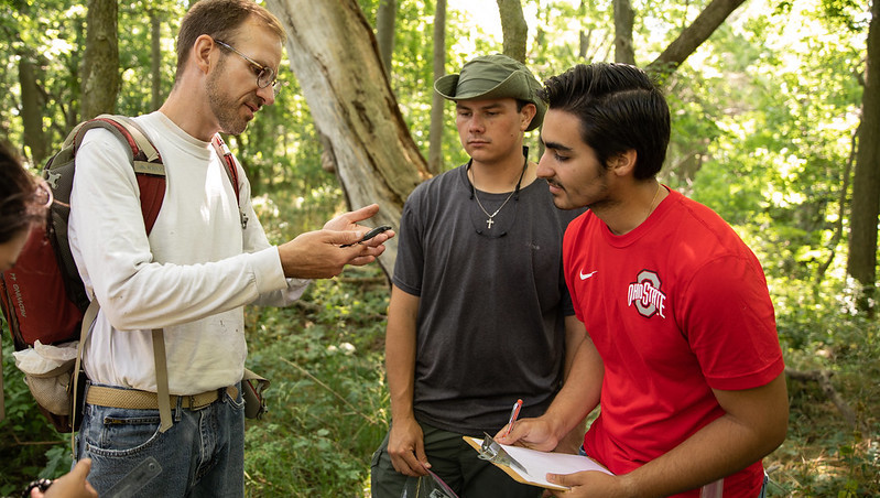 An instructor with two students. He is holding a lizard while the two students listen intently