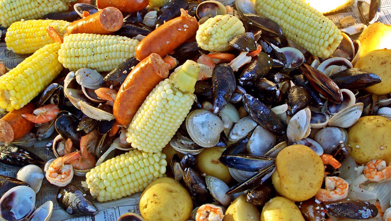 Clam Bake ingredients including corn, potatoes, clams, shrimp, and sausage