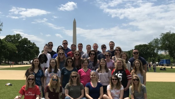 A large group of students standing on a grassy field. Behind them is the Washington Monument