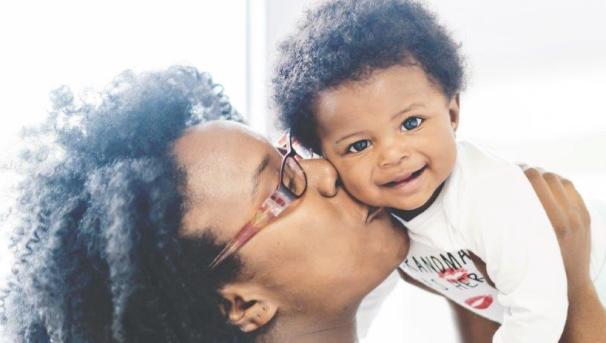 A mother holds her young child up, kissing the side of their cheek