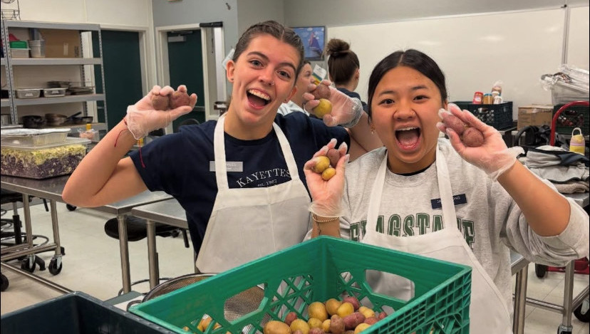 2 kayette members are smiling with their mouths open while holding up small potatoes in their hands.