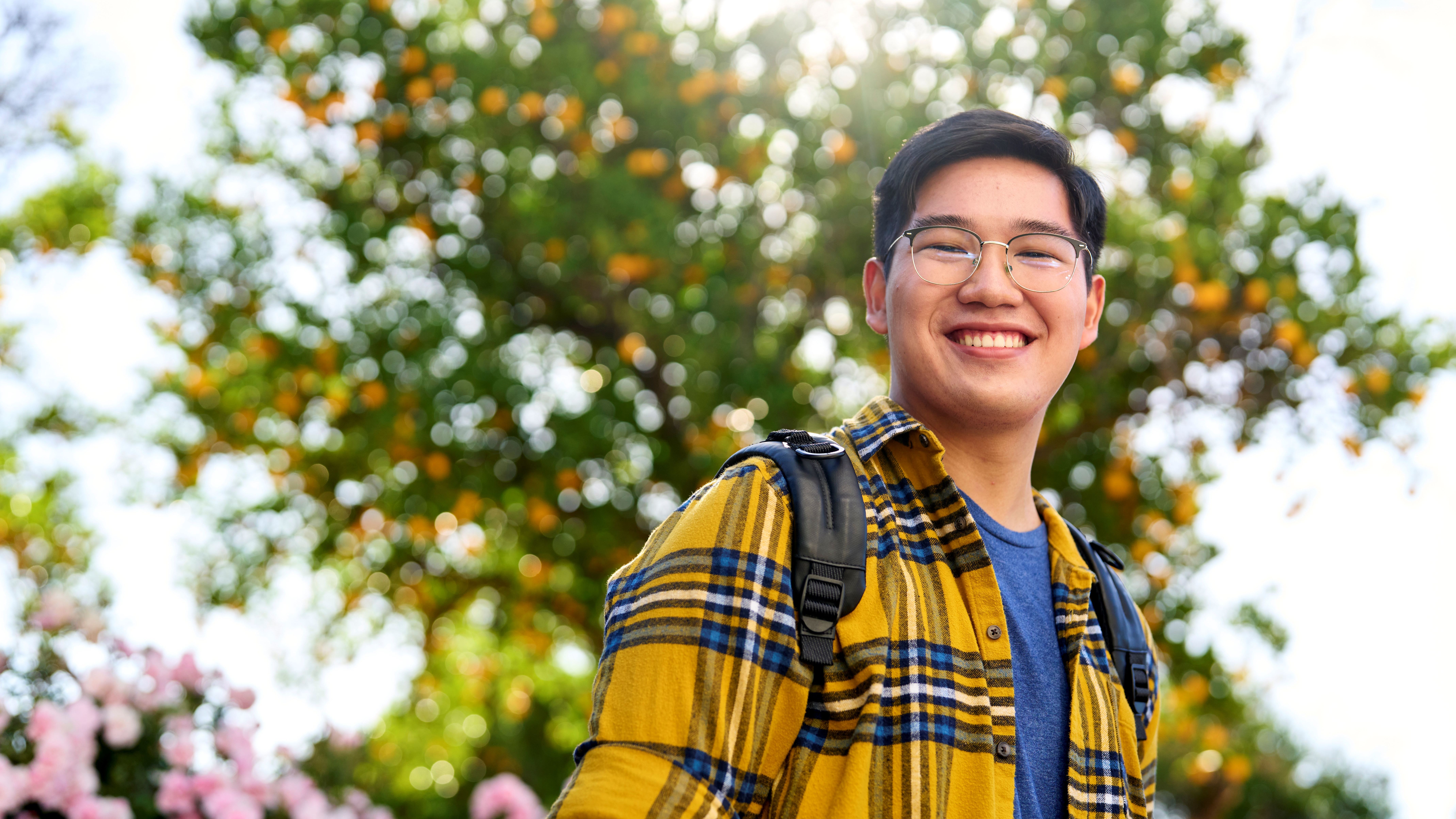 A smiling student wearing glasses, a yellow plaid shirt, and a backpack.