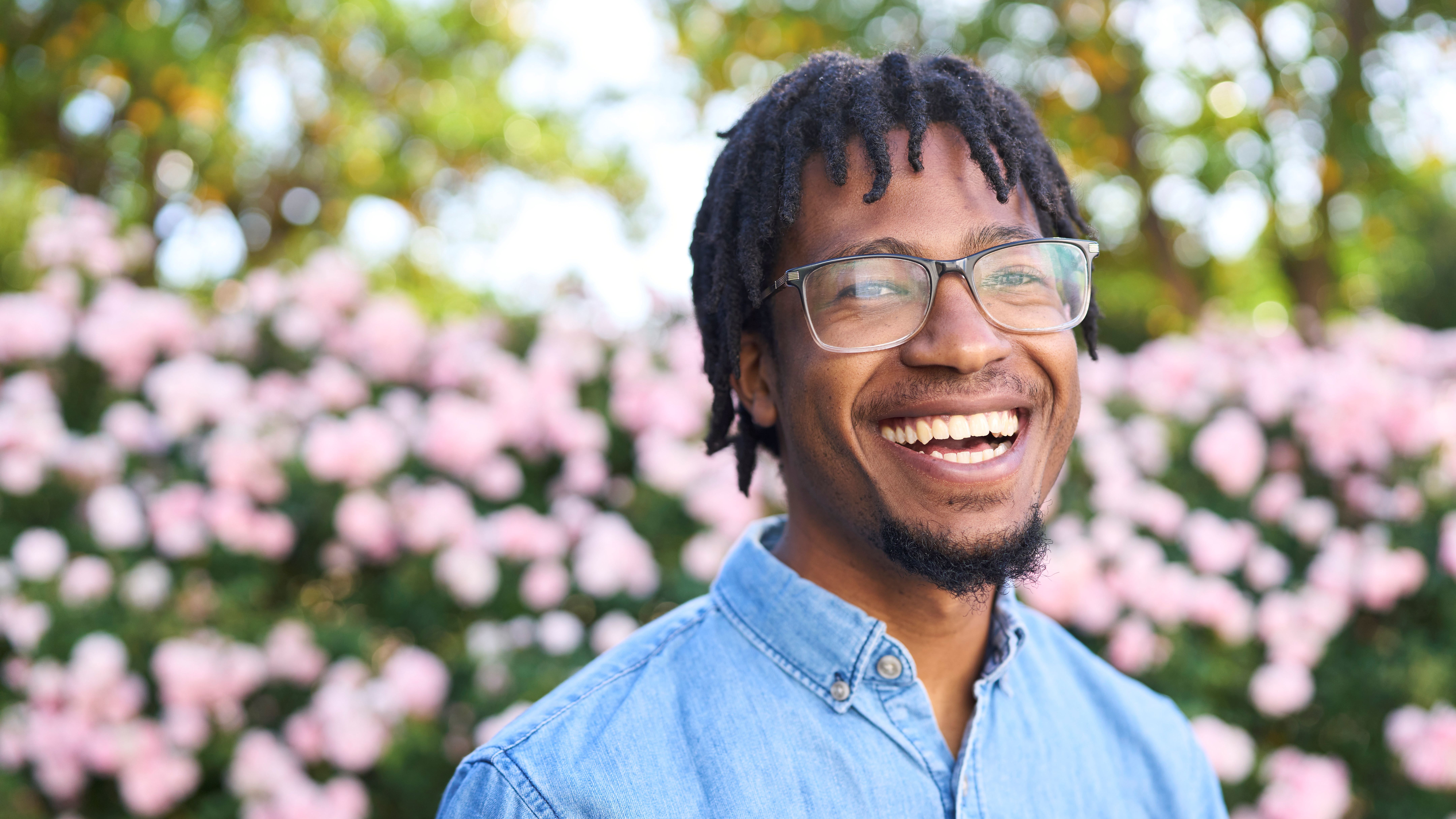A smiling student with glasses, wearing a light blue shirt.