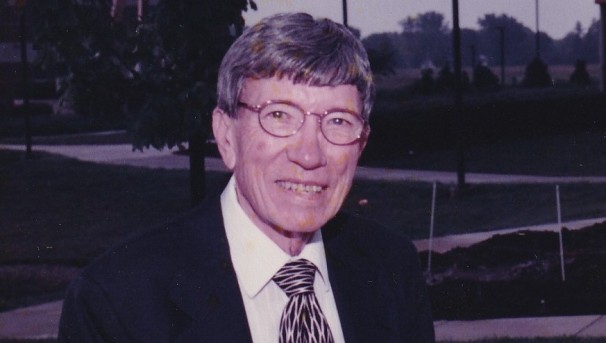 Hal Hazelett standing before a greenery patch, smiling towards the camera
