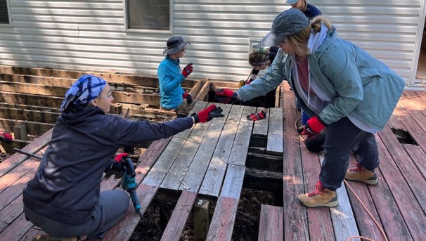 Individuals working on replacing a deck at someone's home outside